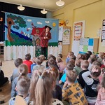 Dzieci siedzą na dywanie i oglądają teatrzyk.