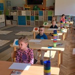 Dzieci siedzą w ławkach i słuchają zadania do wykonania.