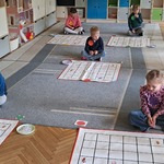 Dzieci siedzą na dywanie i kodują trasę na matach.