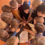 Dzieci stoją w kole_ trzymając ręce nad kartką z napisem „Każdy w grupie 5 jest ważny”..